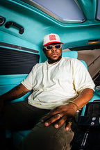 Man wearing a white t-shirt, sunglasses, and a cap sitting inside a turquoise vehicle.