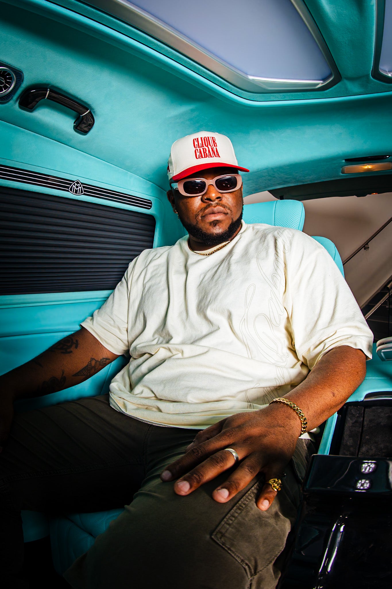 Man wearing a white t-shirt, sunglasses, and a cap sitting inside a turquoise vehicle.